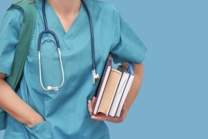 Nursing student in blue scrubs with a stack of books