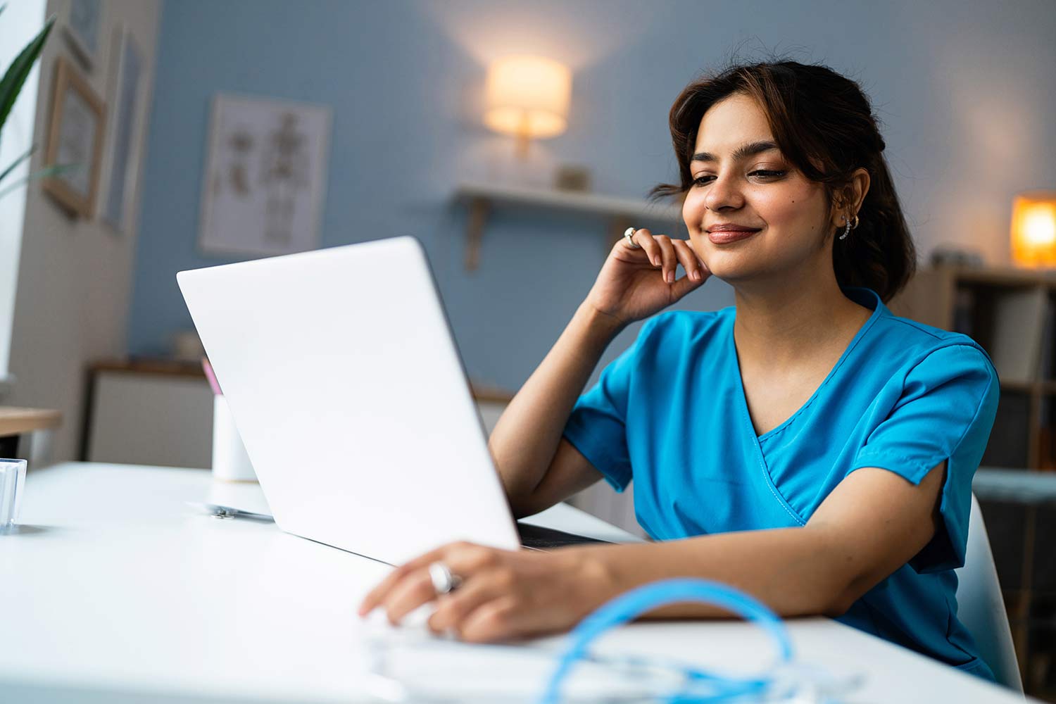 Indian woman in blue scrubs using a laptop